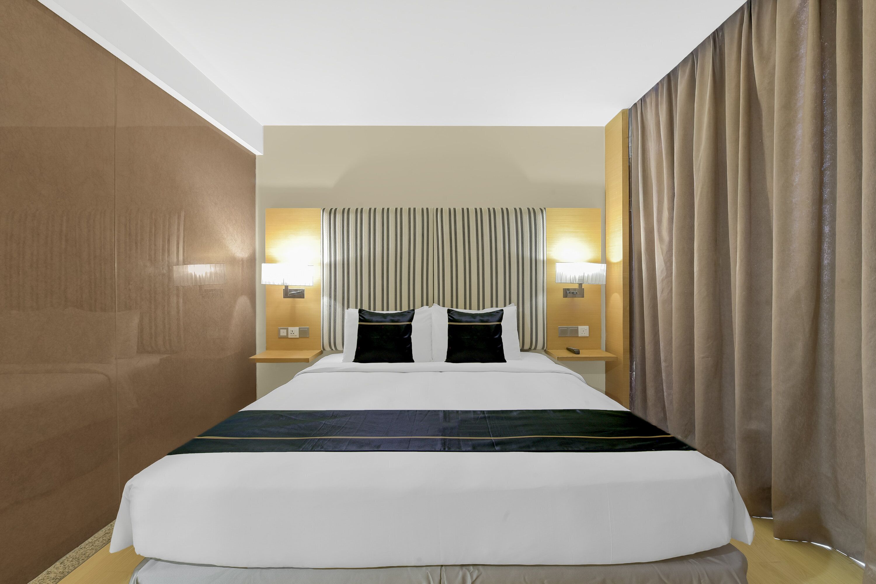 A hotel room with a large bed, two bedside tables with lamps, a headboard with vertical lines, and a curtain on the right side.