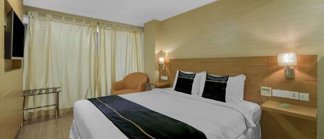 A hotel room with a large bed, a desk, a chair, and a TV mounted on the wall.