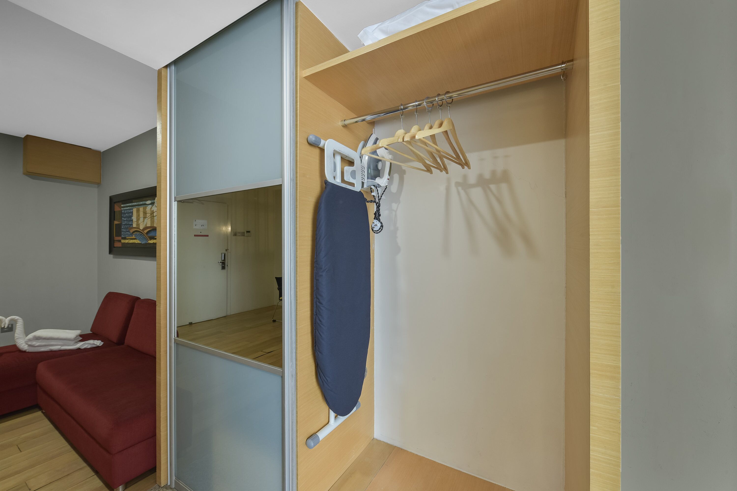 Una habitación de hotel con piso de madera, un sofá rojo, un armario de madera y un espejo.