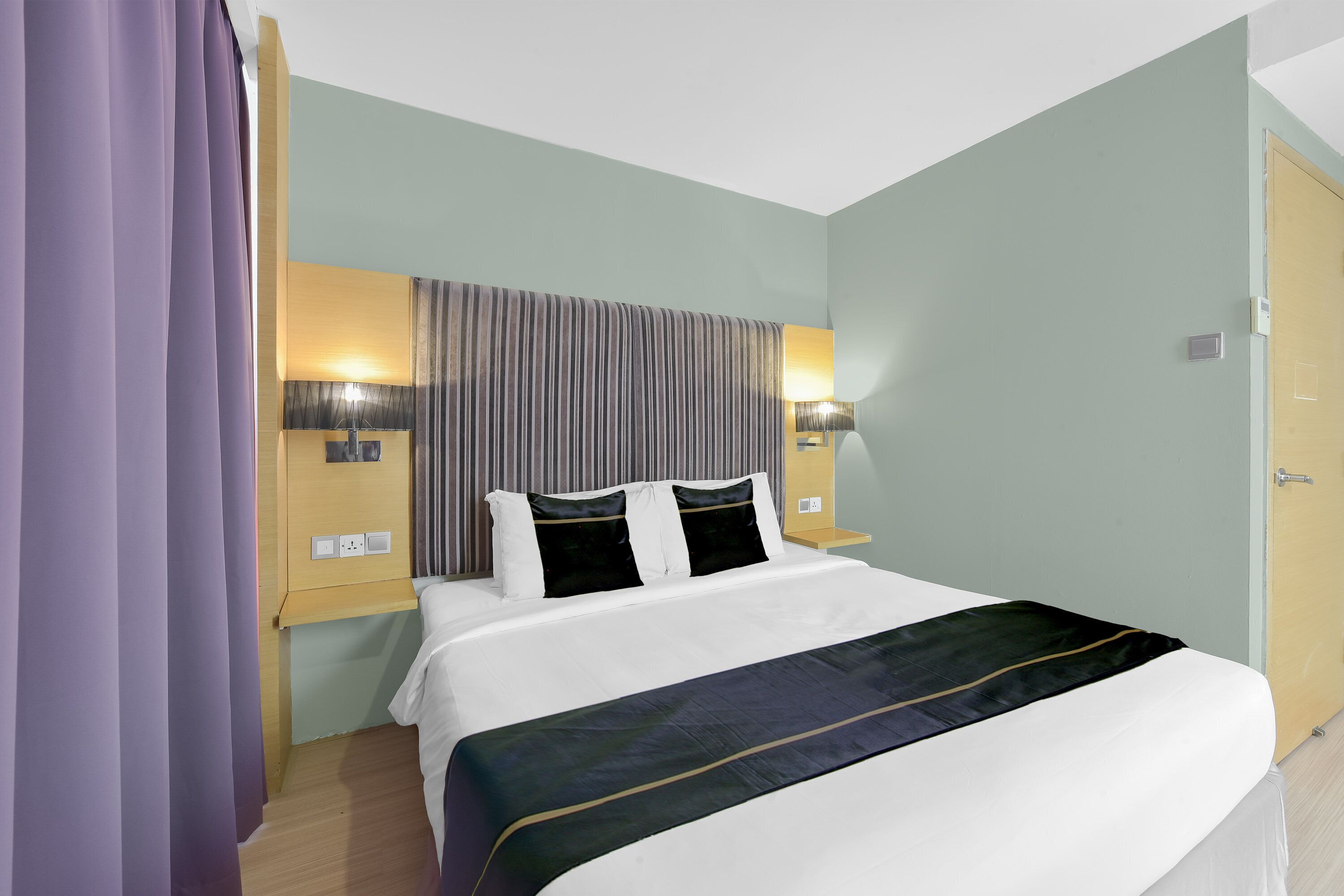 Una habitación de hotel con una cama, dos mesitas de noche, un cabecero y una lámpara de pared.