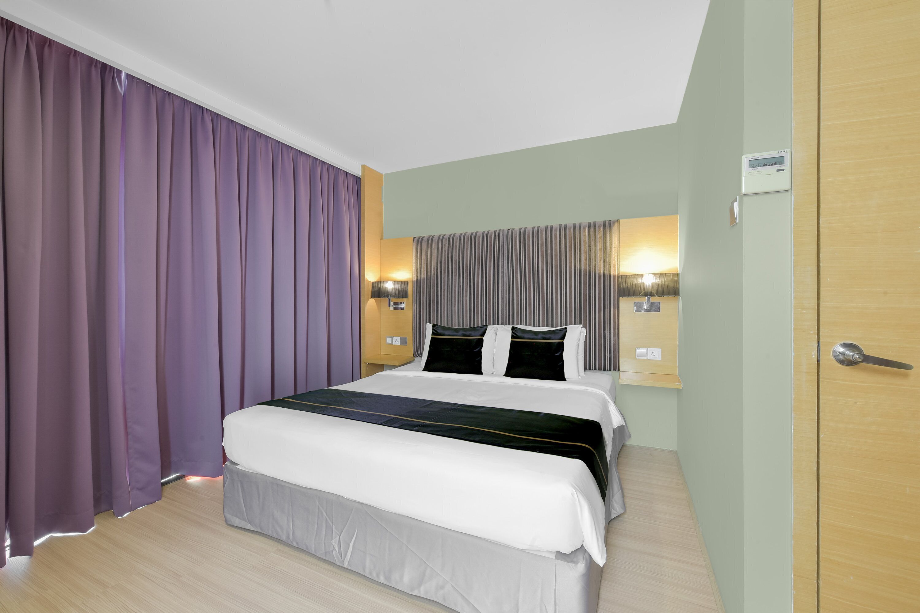 A hotel room with a large bed, a nightstand, a lamp, and a wall-mounted air conditioning unit.