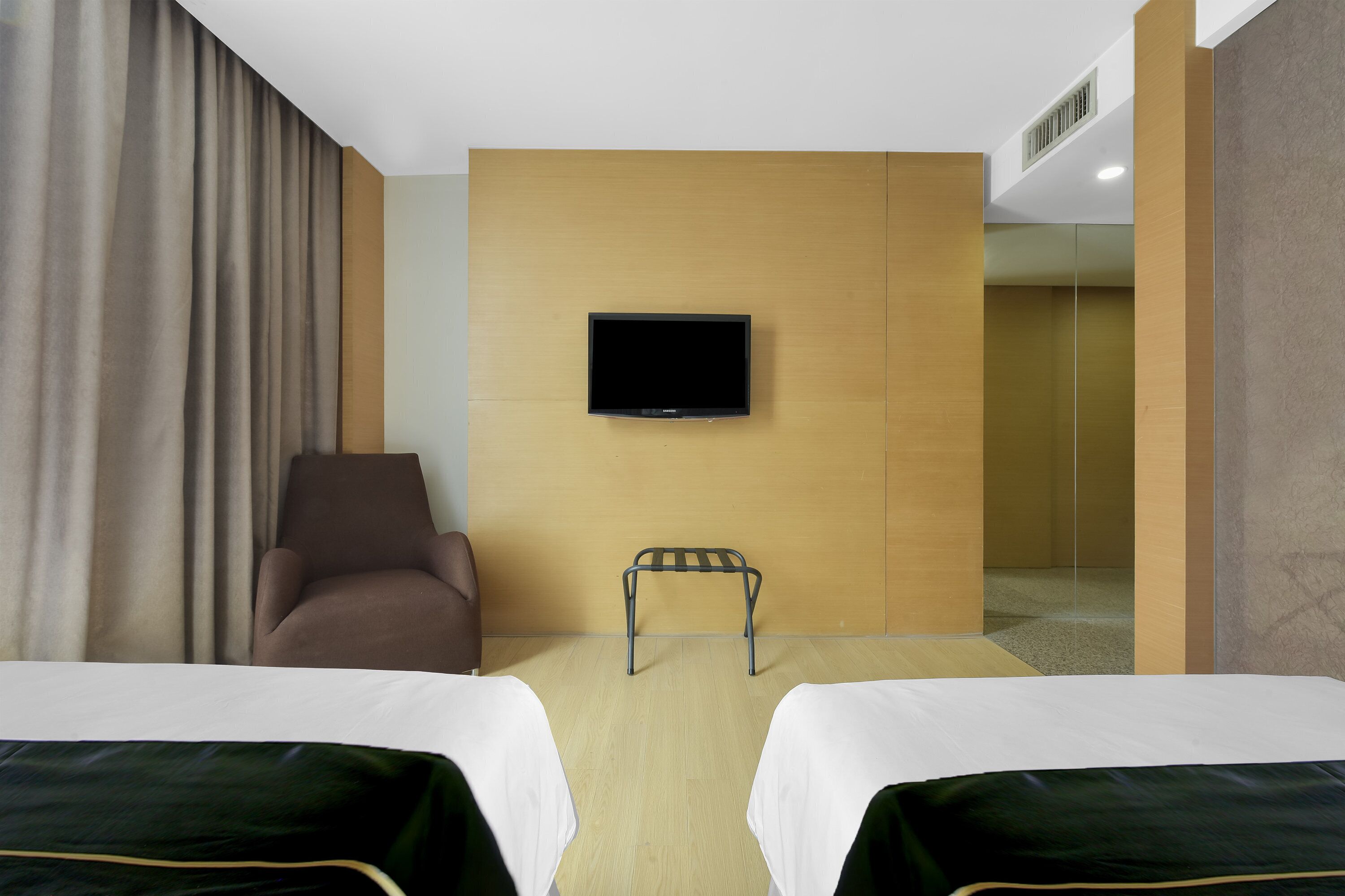 Habitación de hotel con dos camas, un televisor montado en la pared, una silla y una mesita.