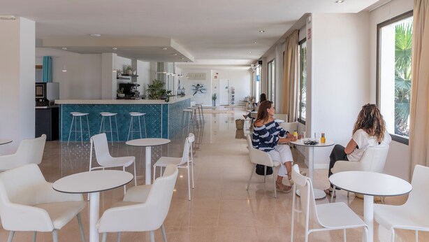 Un hall d’hôtel moderne, doté de meubles blancs, d’un bar central et de grandes fenêtres offrant une vue panoramique.