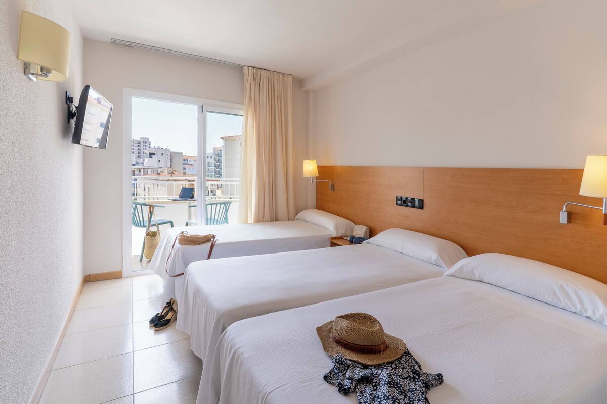 A hotel room with two beds, a balcony, and a city view.