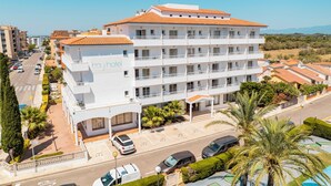 A multi-story hotel with a white facade and orange-tiled roof, featuring balconies and a parking area. - BAY HOTEL (Roses)