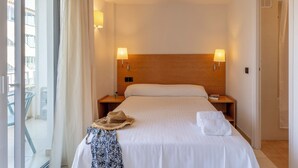A hotel room with a large bed, two bedside lamps, a wooden headboard, a window with curtains, and a view of the outside. - BAY HOTEL (Roses)