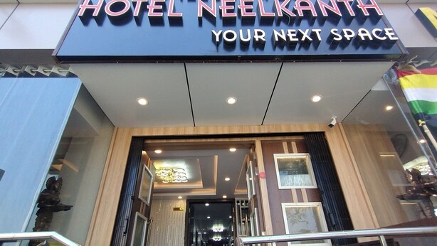 Der Eingang des Hotel Neelkanth mit modernem Design, inklusive einer gut sichtbaren Beschilderung und einer Glastür.