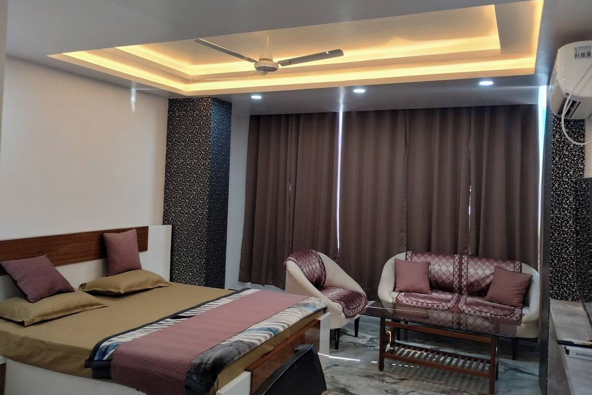 A hotel room with a bed, two armchairs, a ceiling fan, and a large window with curtains.