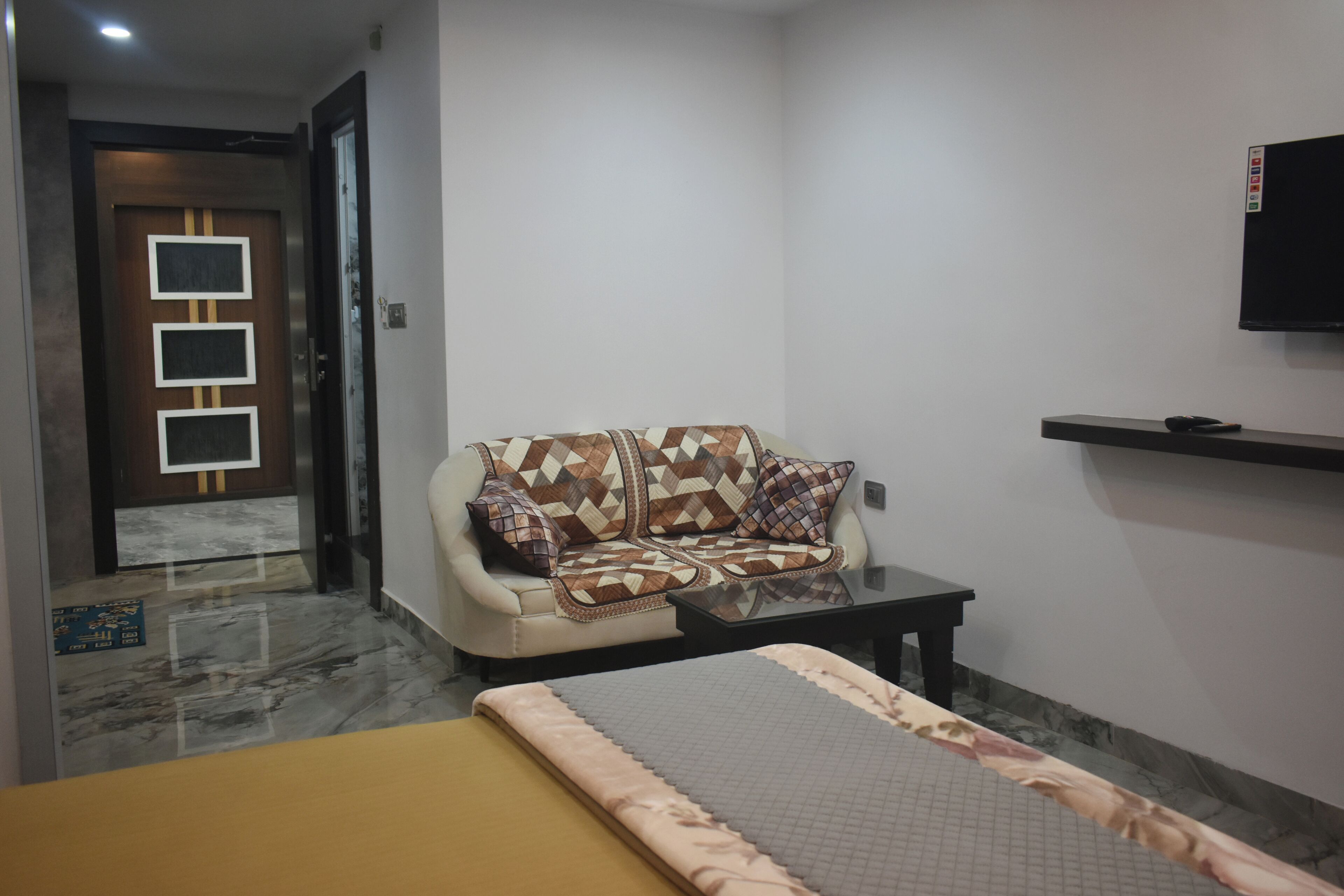 Une chambre d’hôtel avec un canapé, un lit, un téléviseur fixé au mur et une petite table.