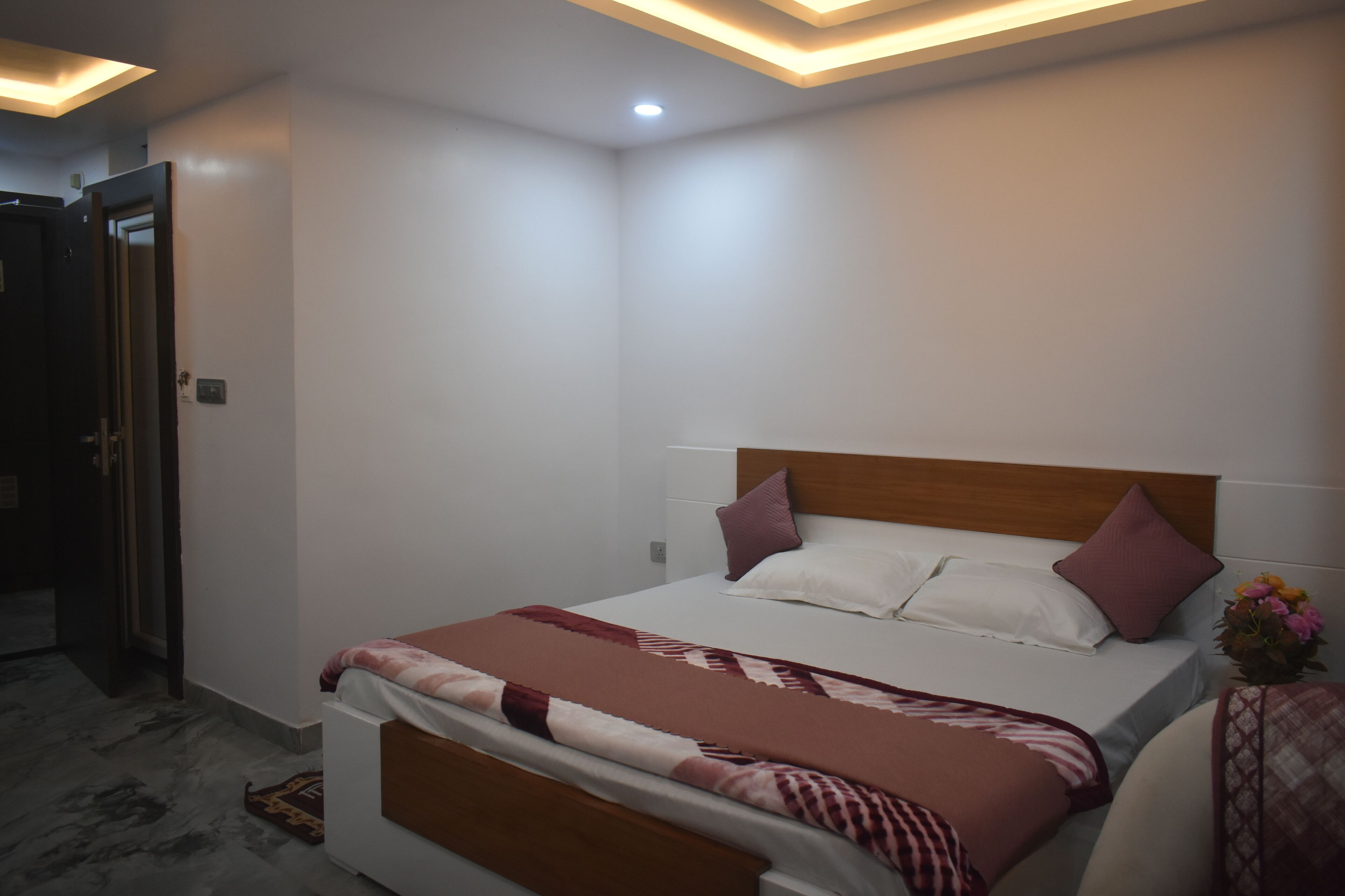 Une chambre à coucher avec un lit, une tête de lit en bois et une table de chevet ornée d’un vase de fleurs.