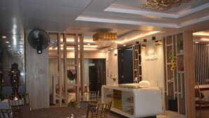 Eine moderne Hotelhalle mit Empfangstresen, Sitzgelegenheiten und dekorativen Elementen wie einem Kronleuchter und Wandventilator.