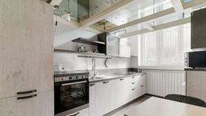 Una cucina moderna con mobili bianchi, elettrodomestici in acciaio inossidabile e una finestra che fa entrare luce naturale.