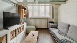 Un soggiorno moderno con una televisione a schermo piatto, mobili contenitori in legno, un divano e una finestra con persiane.