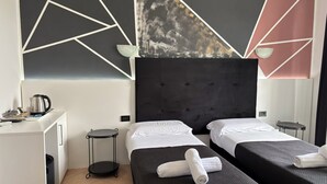 Habitación de hotel con dos camas, un escritorio, un hervidor de agua y una pared con diseños geométricos.