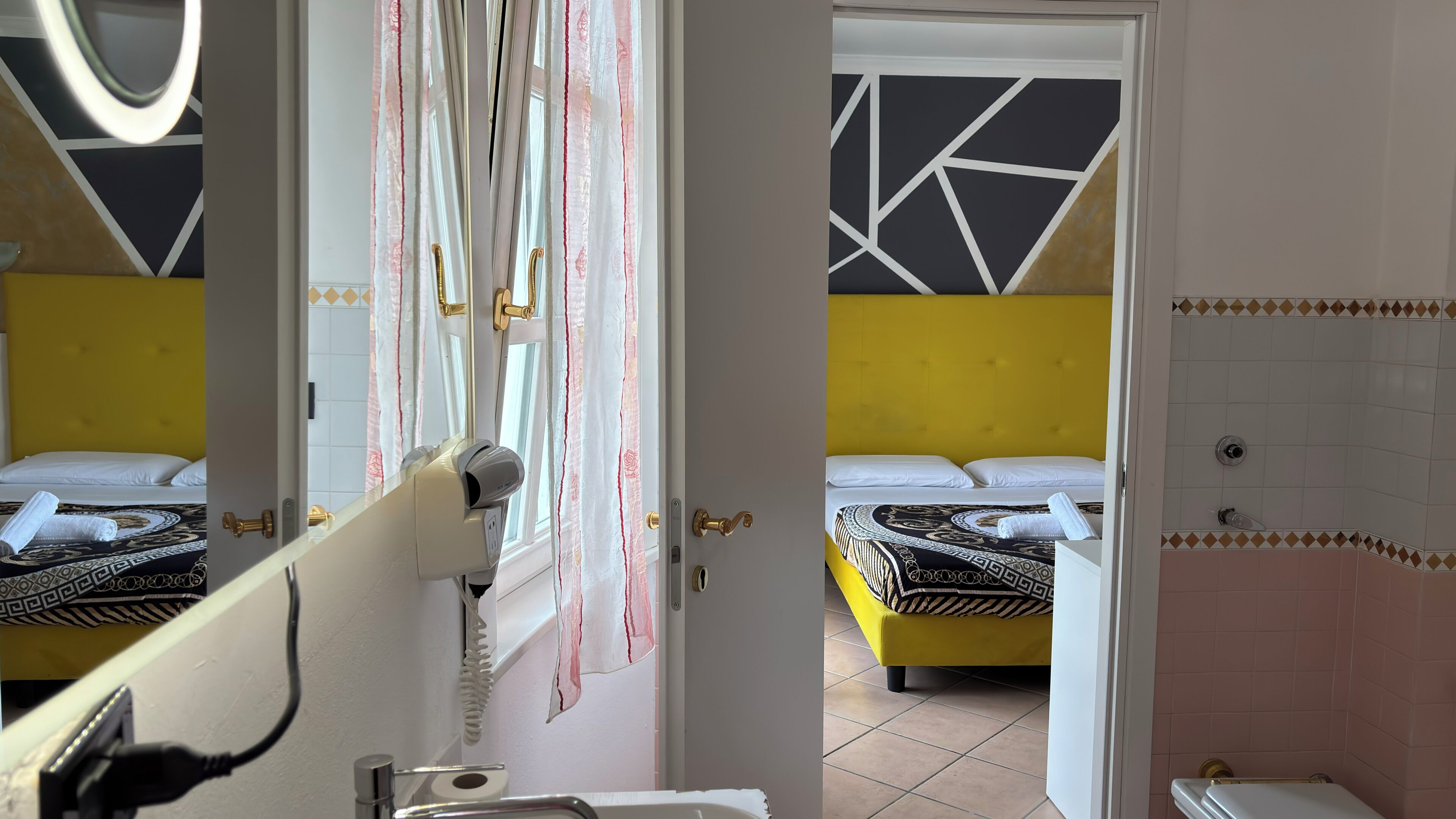 Ein Hotelzimmer mit zwei Betten, einem Badezimmer und einem Spiegel, der den Raum reflektiert.