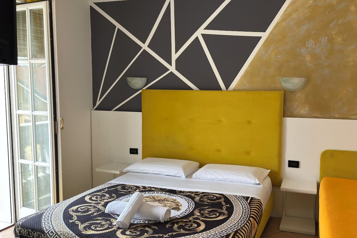 A hotel room with a bed, a yellow headboard, a bedside table, and a small orange chair.