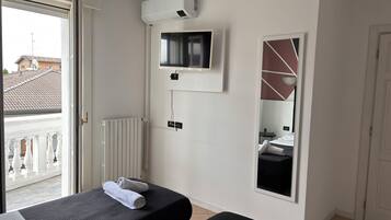 A hotel room with a bed, a TV, a mirror, and a radiator.