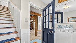 Una escalera con escalones de madera y tapetes azules, una puerta azul oscuro con un letrero que dice 'BEACH', y un pasillo que conduce a una habitación.