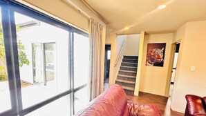 En rummelig opholdsstue med en stor skydedør til en balkon, en trappe og en rød lædersofa.