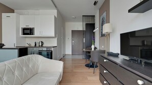 A modern living room with a sofa, a TV, and a kitchen area with cabinets and appliances. - Kwartał Kamienic by Downtown Apartments (Gdańsk)