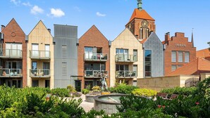 A row of modern buildings with a central tower featuring a clock and a statue. - Kwartał Kamienic by Downtown Apartments (Gdańsk)