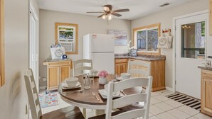 A kitchen with a ceiling fan, a refrigerator, wooden cabinets, a dining table with chairs, and a window with a view.