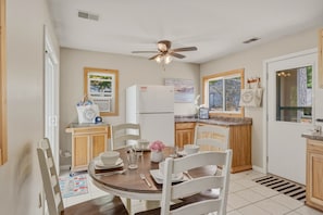 A kitchen with a ceiling fan, a refrigerator, wooden cabinets, a dining table with chairs, and a window with a view.