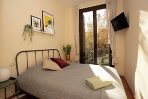 A bedroom with a bed, a TV mounted on the wall, a window with curtains, and a plant on a side table. - Fabulous 2-Bedroom Apartment Eixample (Barcelona)