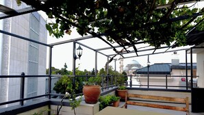 A covered outdoor area with a table and benches, surrounded by potted plants and a view of a building with a dome. - Hotel Öncü (İstanbul)