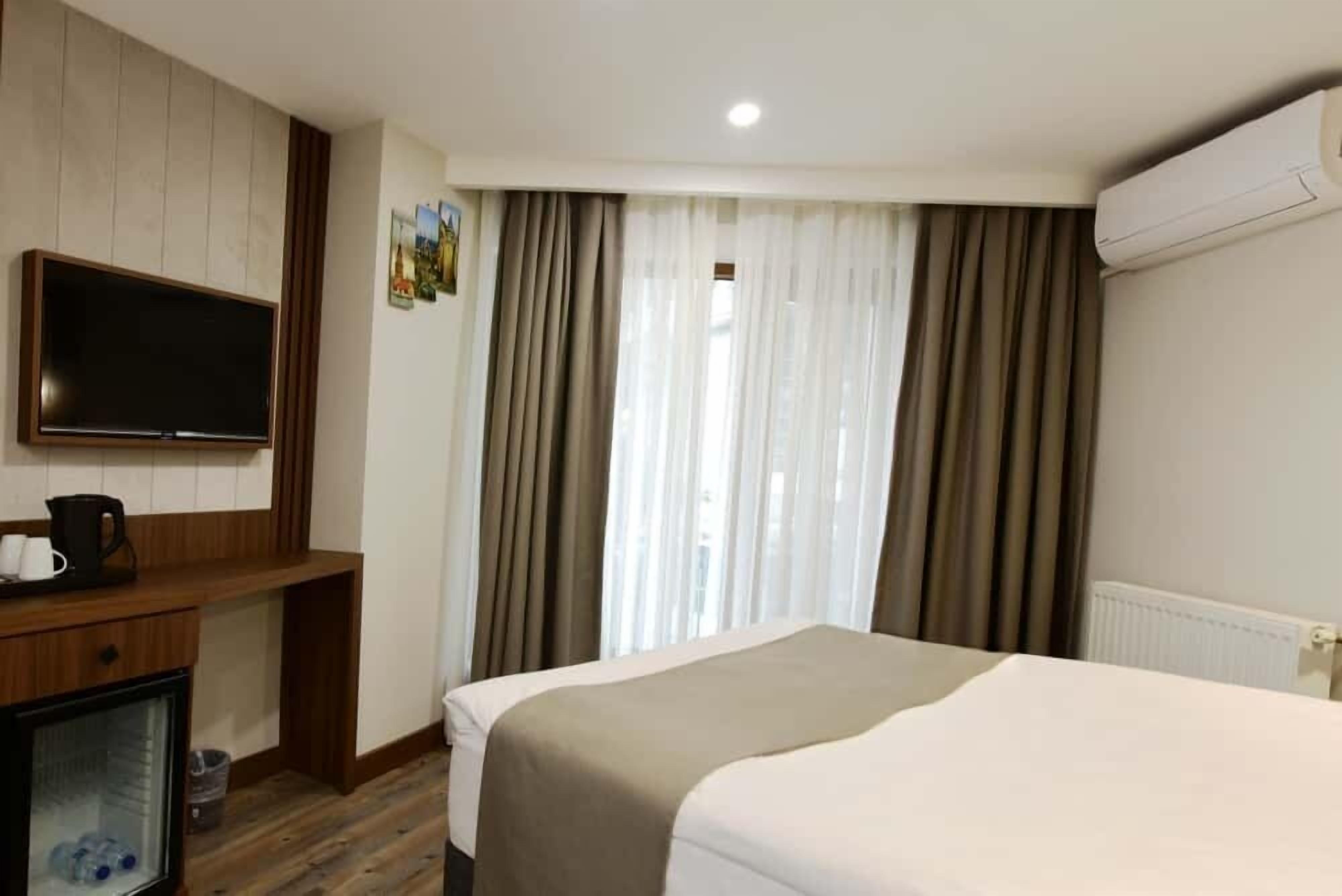 A hotel room with a bed, a TV mounted on the wall, a desk with a coffee maker, and a window with curtains.