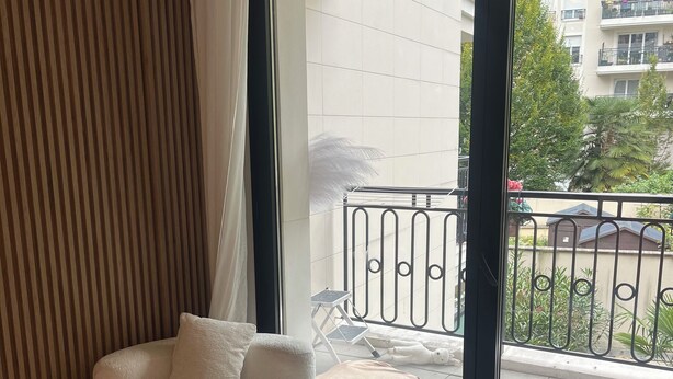 Un soggiorno moderno con una grande finestra, un divano, un tavolino da caffè e vista sul balcone esterno.