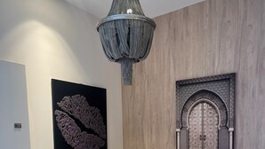 Un tavolo da pranzo rotondo con piano in marmo, circondato da quattro sedie imbottite rosa con gambe in metallo. Sopra il tavolo, un lampadario con finitura metallica. Al muro, un'opera d'arte astratta di grandi dimensioni e un pannello decorativo ad arco.