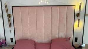 Un letto con testiera, due cuscini, un comodino con una lampada e un punto luce a parete.
