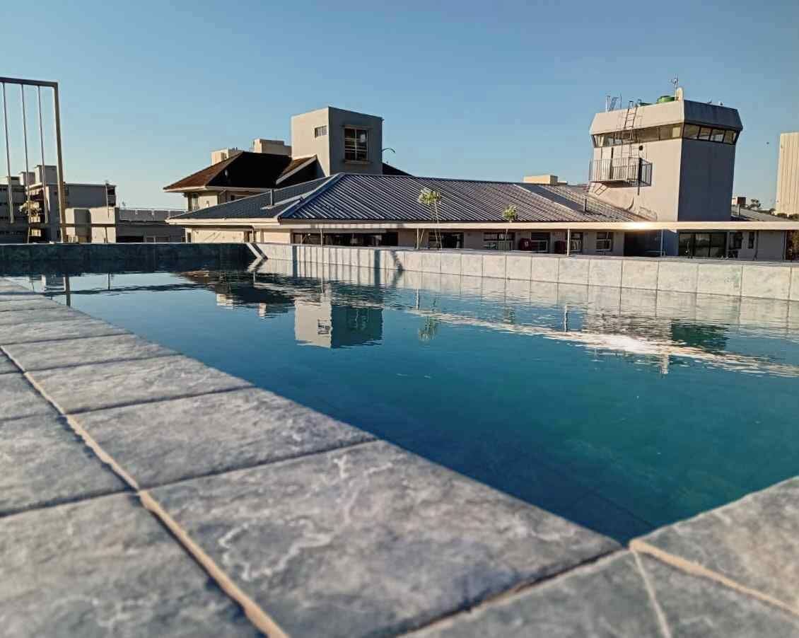 A swimming pool with a tiled edge, a building with a modern architectural style, and a clear sky.
