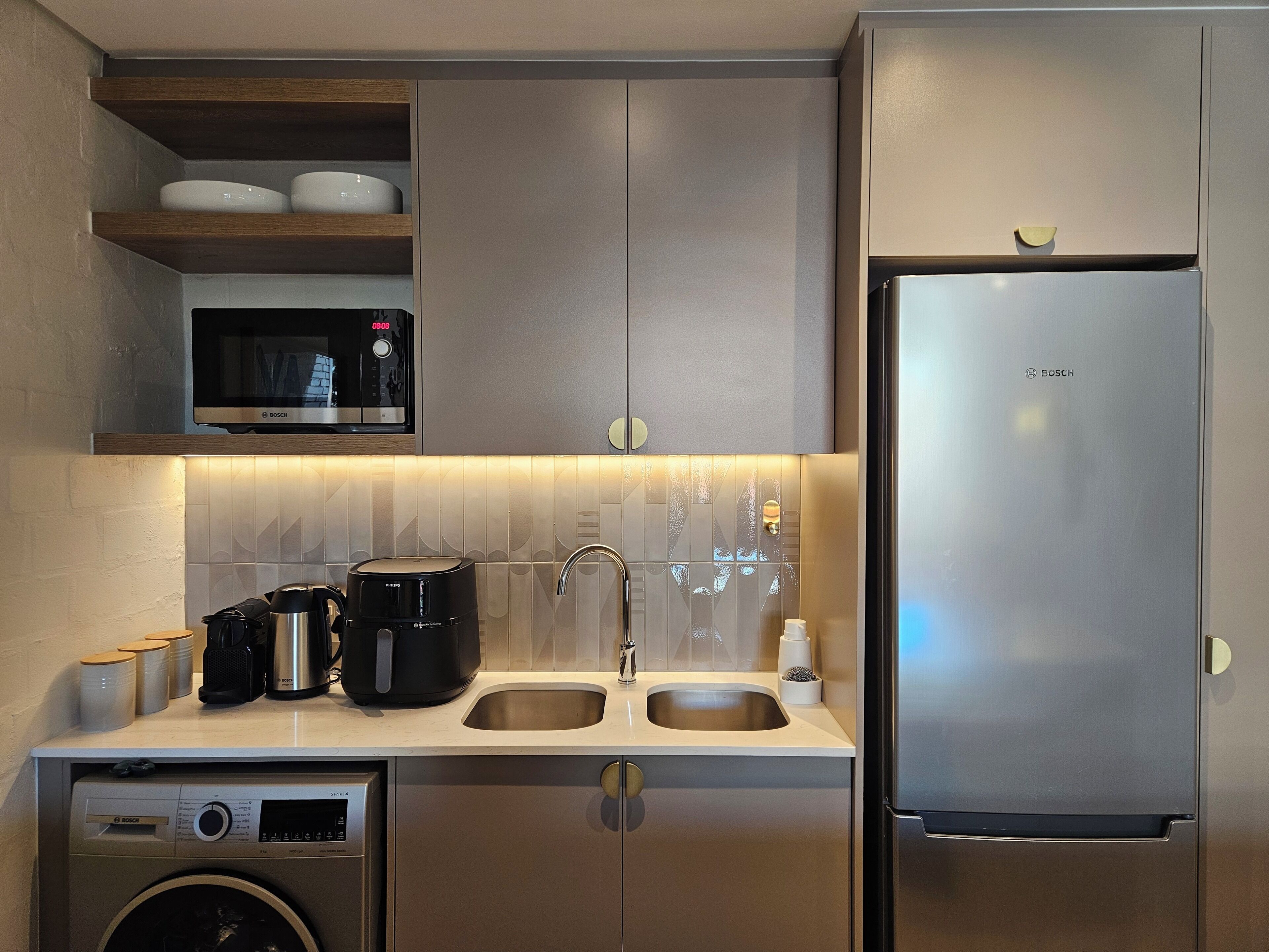 A modern kitchen with stainless steel appliances, including a Bosch microwave, coffee maker, and refrigerator, and a built-in washing machine.