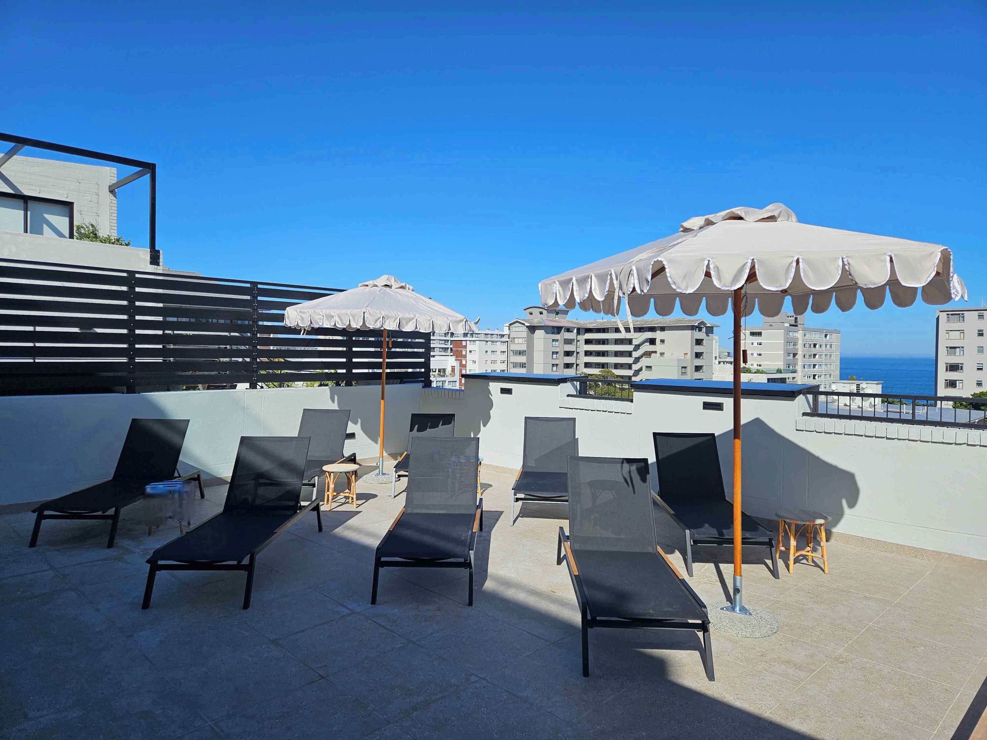 A rooftop terrace with lounge chairs and umbrellas, overlooking a coastal cityscape.