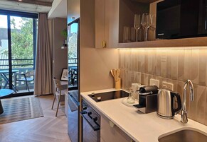 Una cocina moderna con horno empotrado, fregadero y cafetera. Se ve un área de comedor con una mesa y sillas a través de una puerta de cristal.