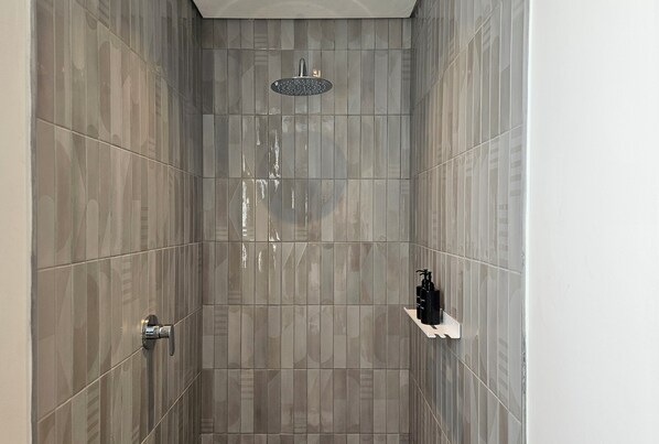 A modern shower with a handheld showerhead, a wall-mounted control, and a small shelf with toiletries. - ONE46 on M - Fluent Serviced Apartments (Cape Town)