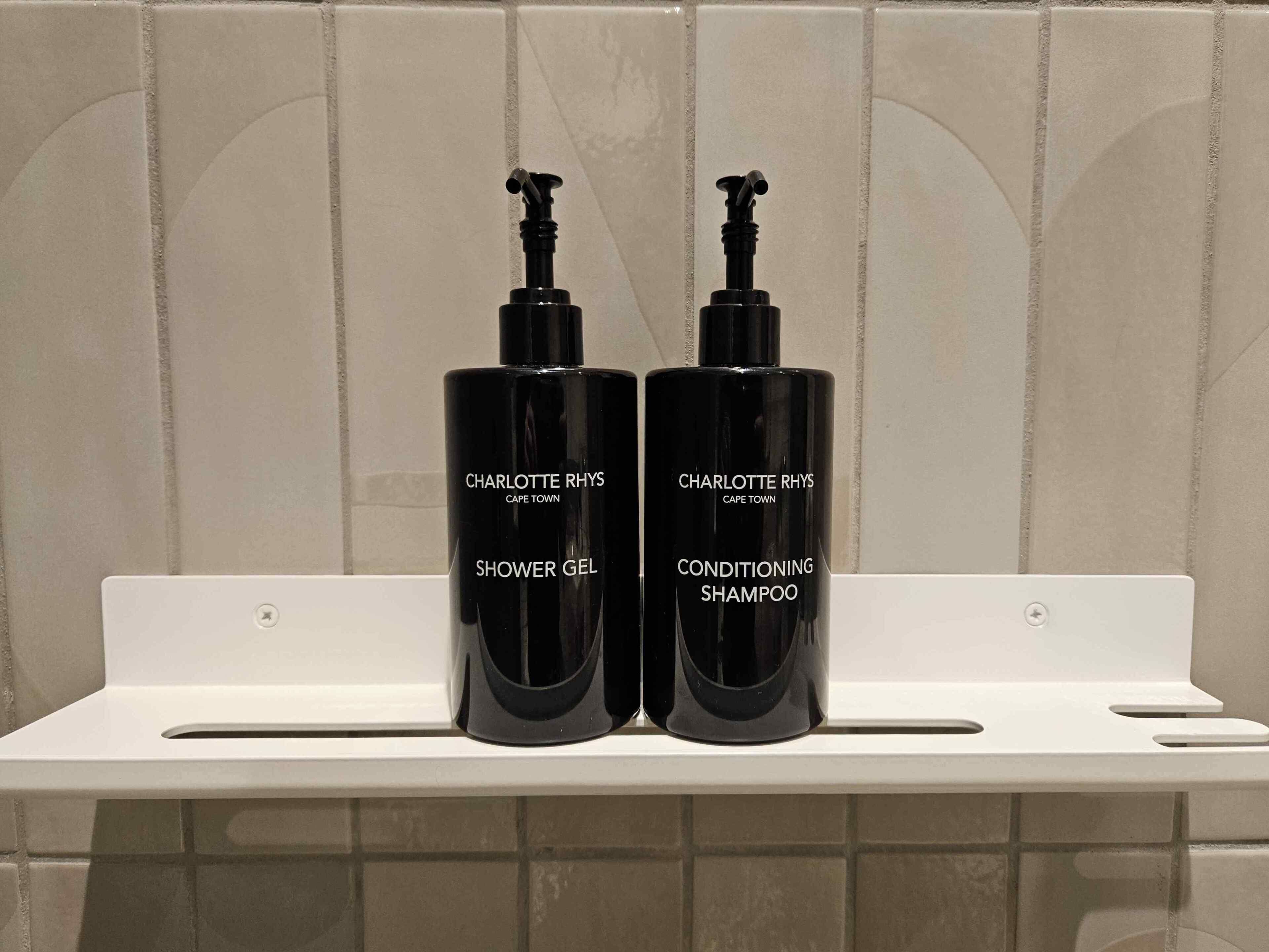 To sorte flasker med Charlotte Rhys produkter på en hvid reol.