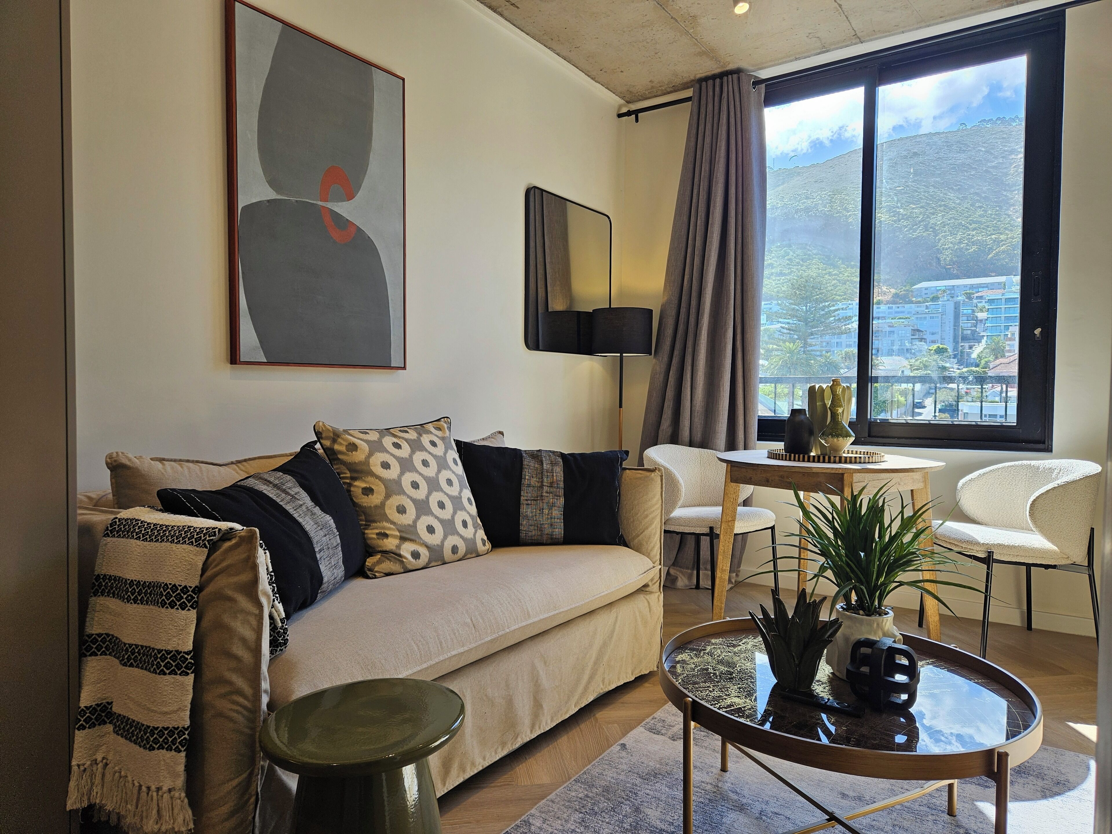 Un salon moderne avec un canapé, une table basse, une lampe et une vue sur le paysage urbain, visible à travers de grandes fenêtres.