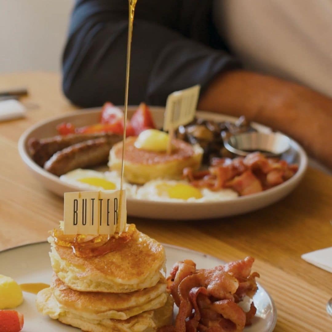 Un piatto per la colazione con pancake, bacon e un cartello che indica il burro.