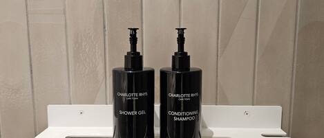 Two black bottles of Charlotte Rhys products on a white shelf against a tiled wall.