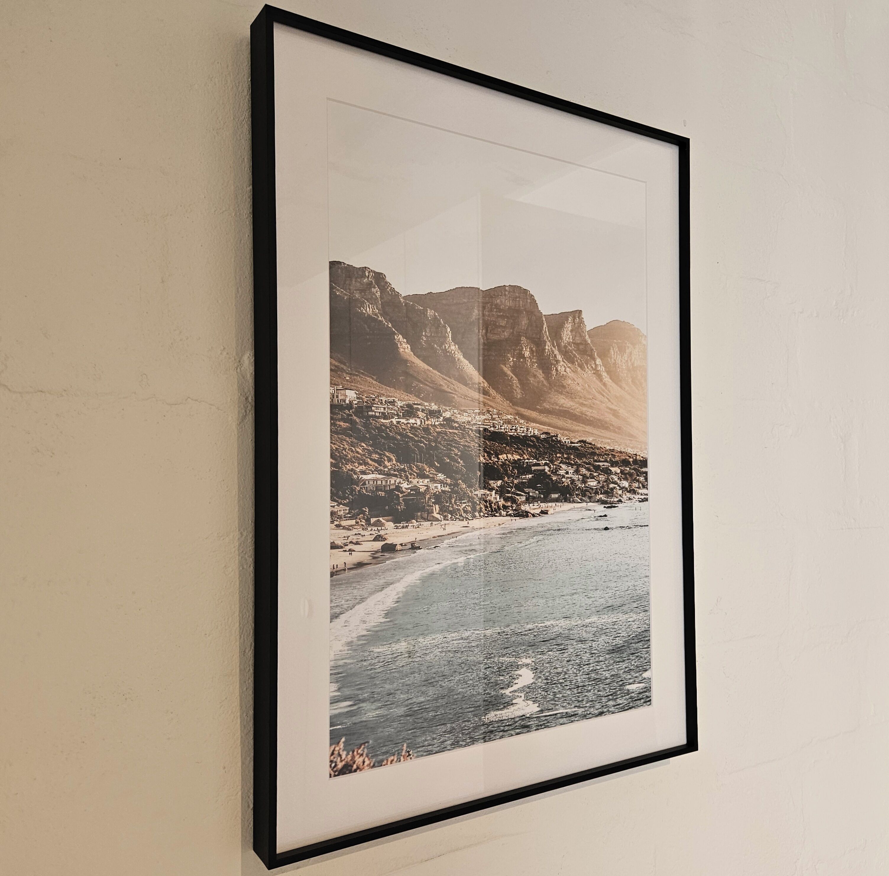 A framed photograph of a mountainous landscape with a river and buildings.