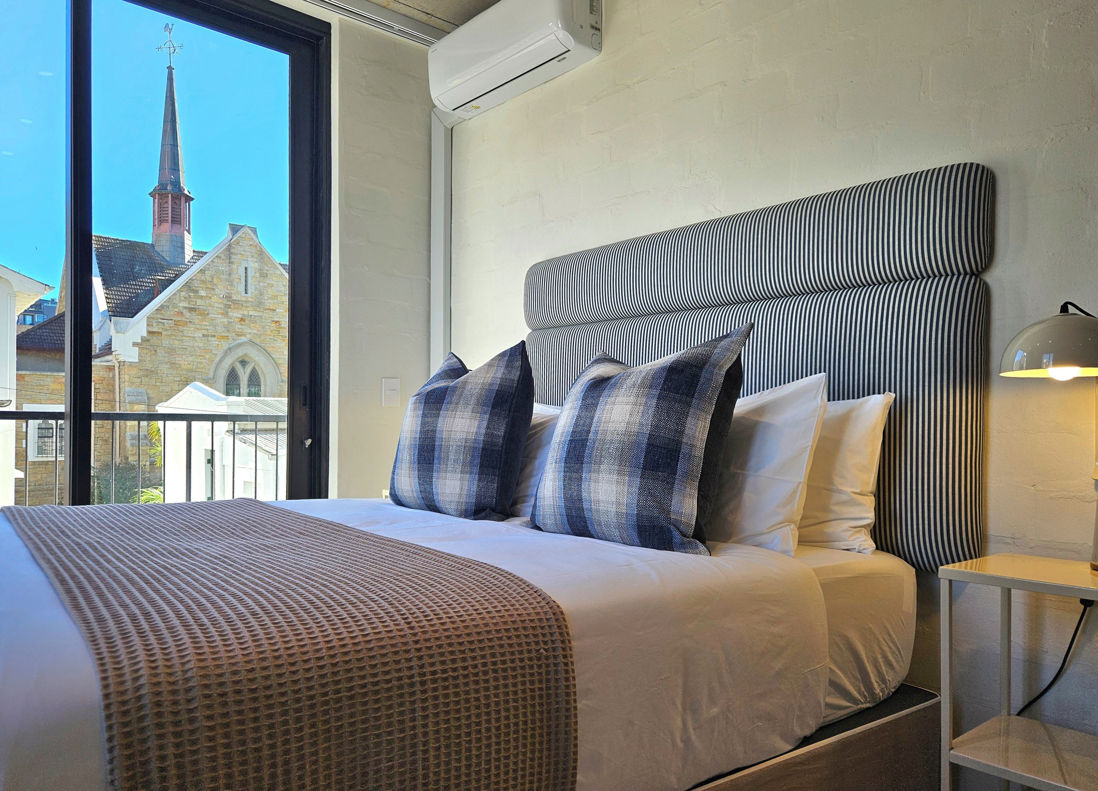 A hotel room with a large bed, a view of a church steeple, and a modern lamp.