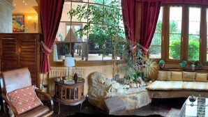 A cozy room with a stone fireplace, a bench with plants, and a view of greenery outside. - Royal Suite (Mungia)