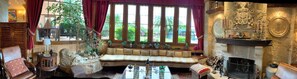 A cozy room with a stone fireplace, a bench with plants, and a view of greenery outside. - Royal Suite (Mungia)