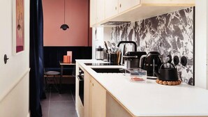 A compact kitchen with a white countertop, black kettle, and a marble backsplash.