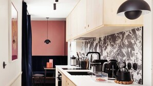 A compact kitchen with a central island, black pendant lighting, and a marble backsplash.
