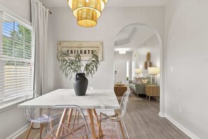 A dining area with a marble table, clear chairs, a vase with a plant, and a sign reading "TAILGATE". - Sweet Olive | Stylish 3BR Near UA • Fire Pit (Northport)