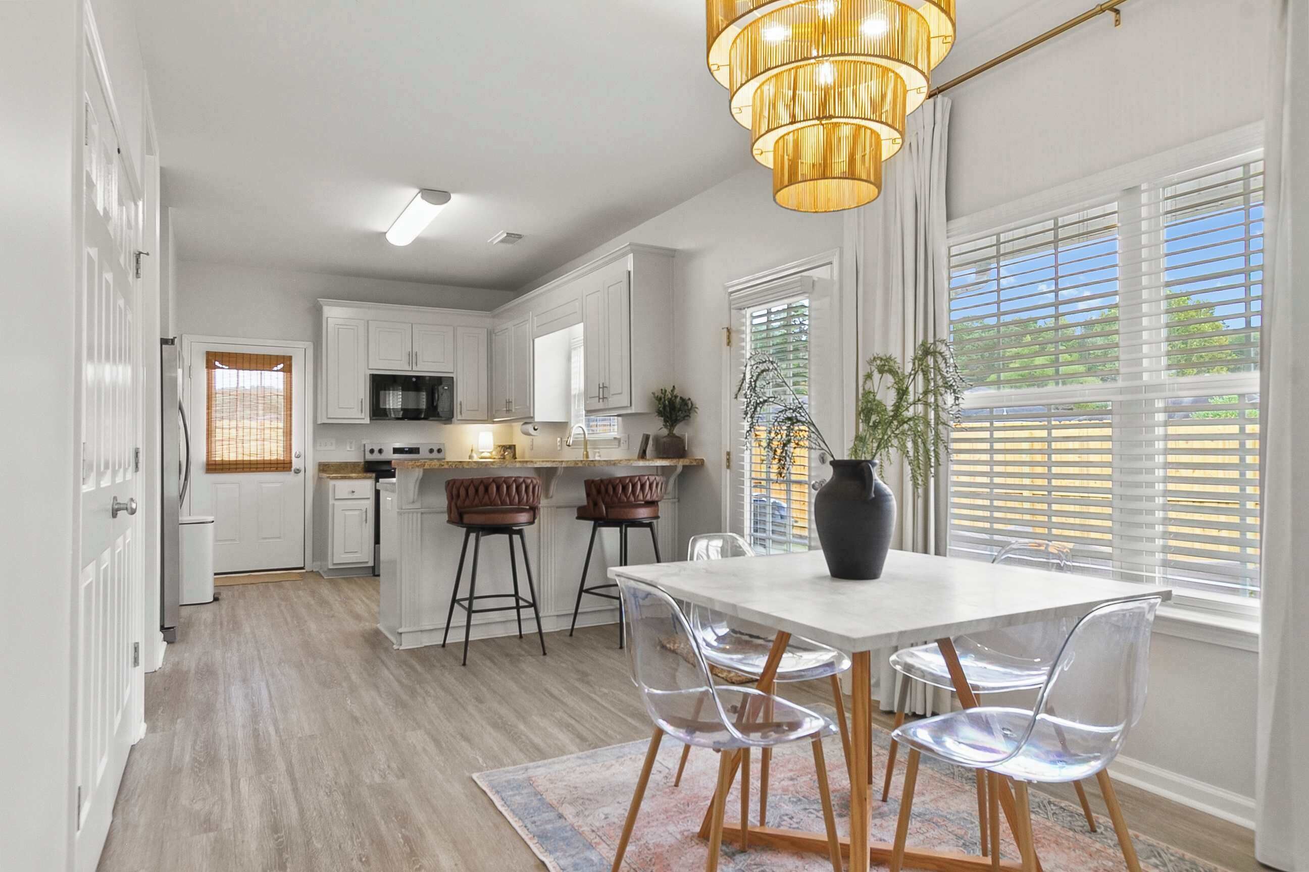 A modern kitchen with white cabinets, a central island, bar stools, and a dining table with clear chairs.